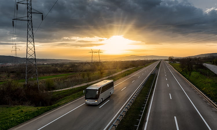 A charter bus drives at sunset on an empty highway